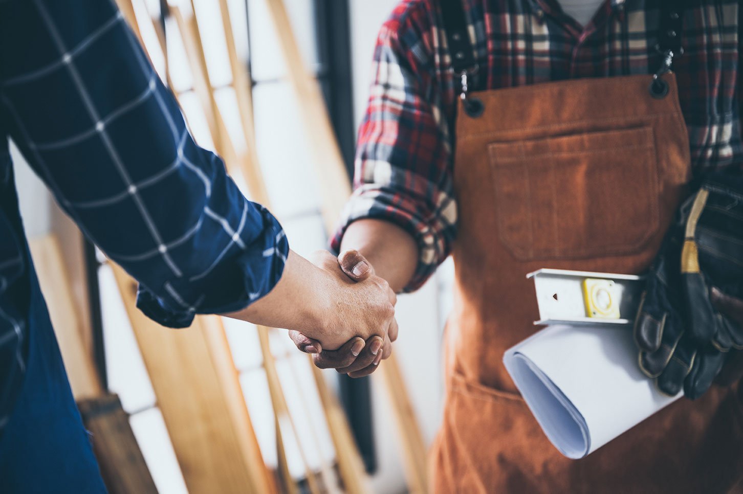 man wearing overalls, carrying tools and shaking hands with another man